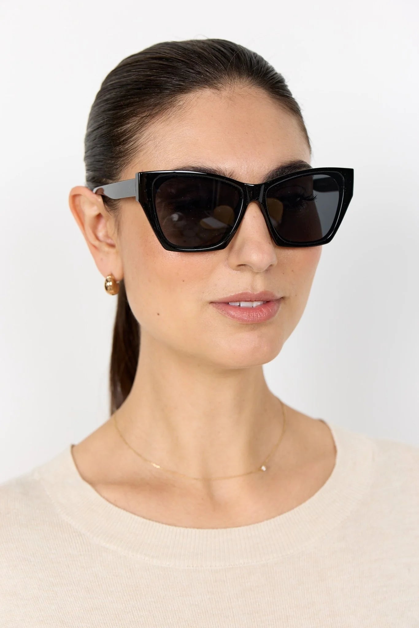 Woman wearing black cat-eye sunglasses against a white background