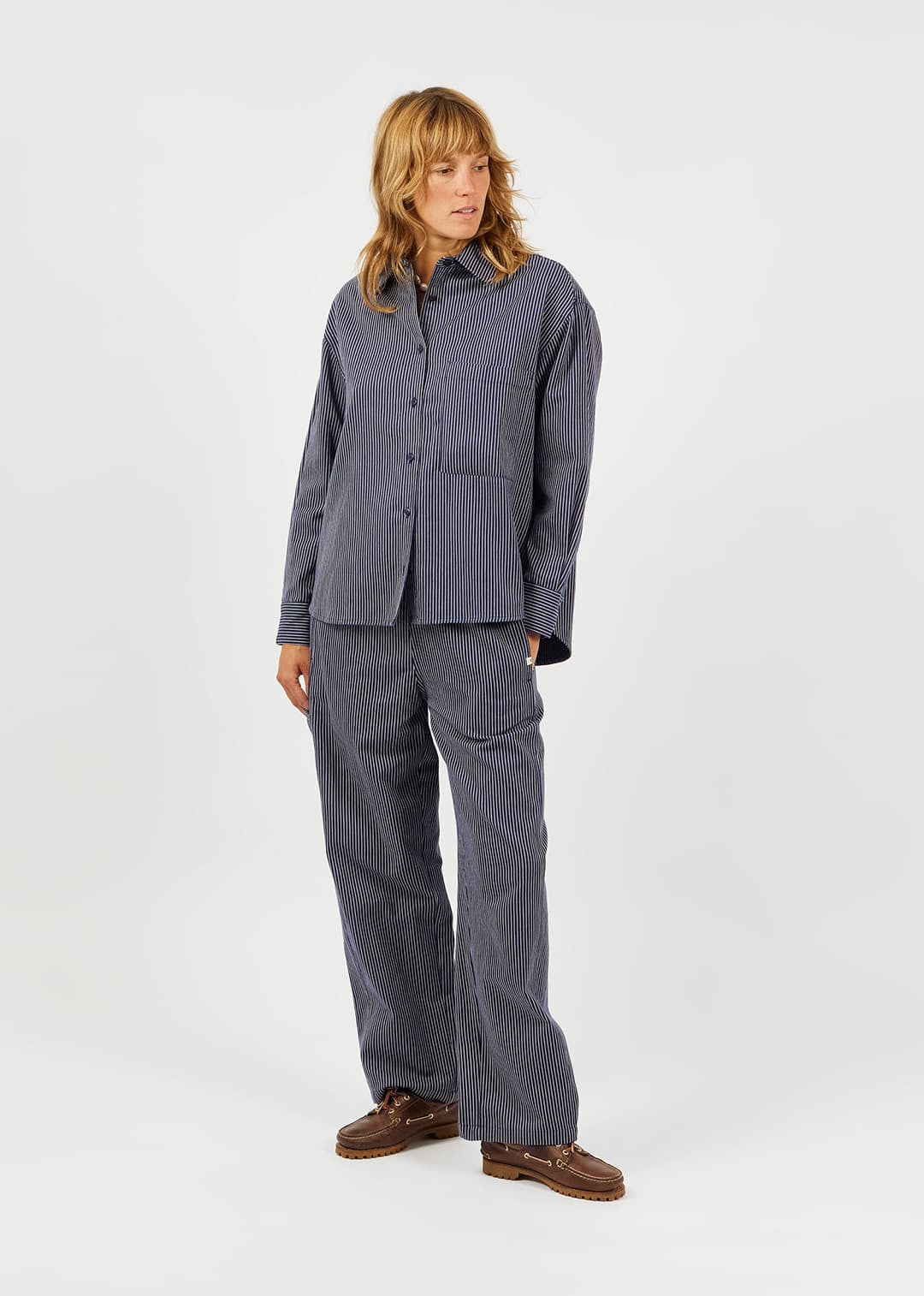A model wearing a matching gray corduroy lounge set consisting of a long-sleeve button-up shirt and wide-leg trousers, paired with brown leather shoes, against a plain light gray background.