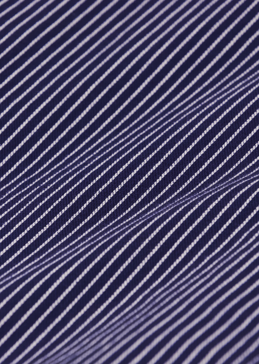 A close-up of a navy blue fabric with thin, evenly spaced white diagonal stripes, showing a soft drape and woven texture.