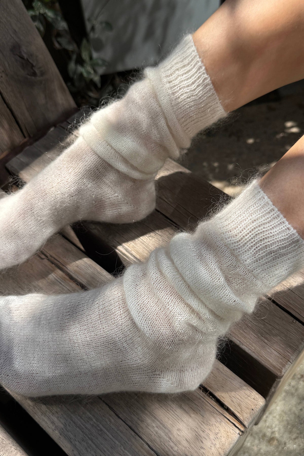A close-up of a person's feet wearing fluffy, off-white knit socks while sitting on weathered wooden steps outdoors.
