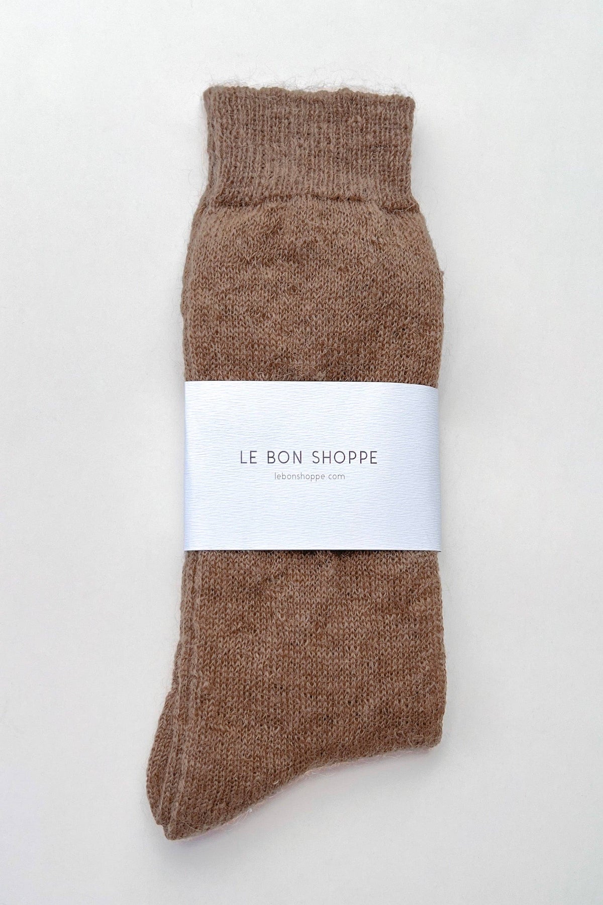 A single brown knit sock with a white paper band reading 'LE BON SHOPPE' wrapped around the middle, photographed on a plain light background.