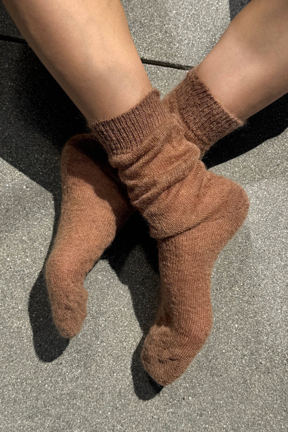 A pair of cozy, ribbed ankle socks in a warm brown color, worn on feet resting on a gray textured concrete surface.