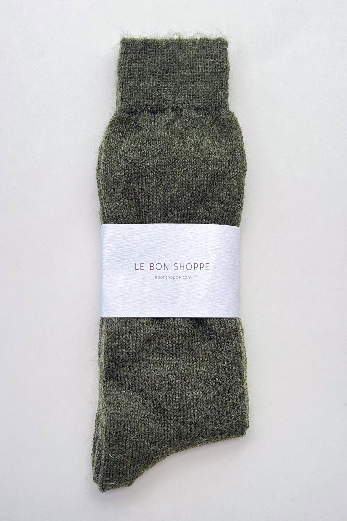 A single dark olive green knit sock with a white paper band around the middle that reads 'LE BON SHOPPE', photographed flat against a light gray background.