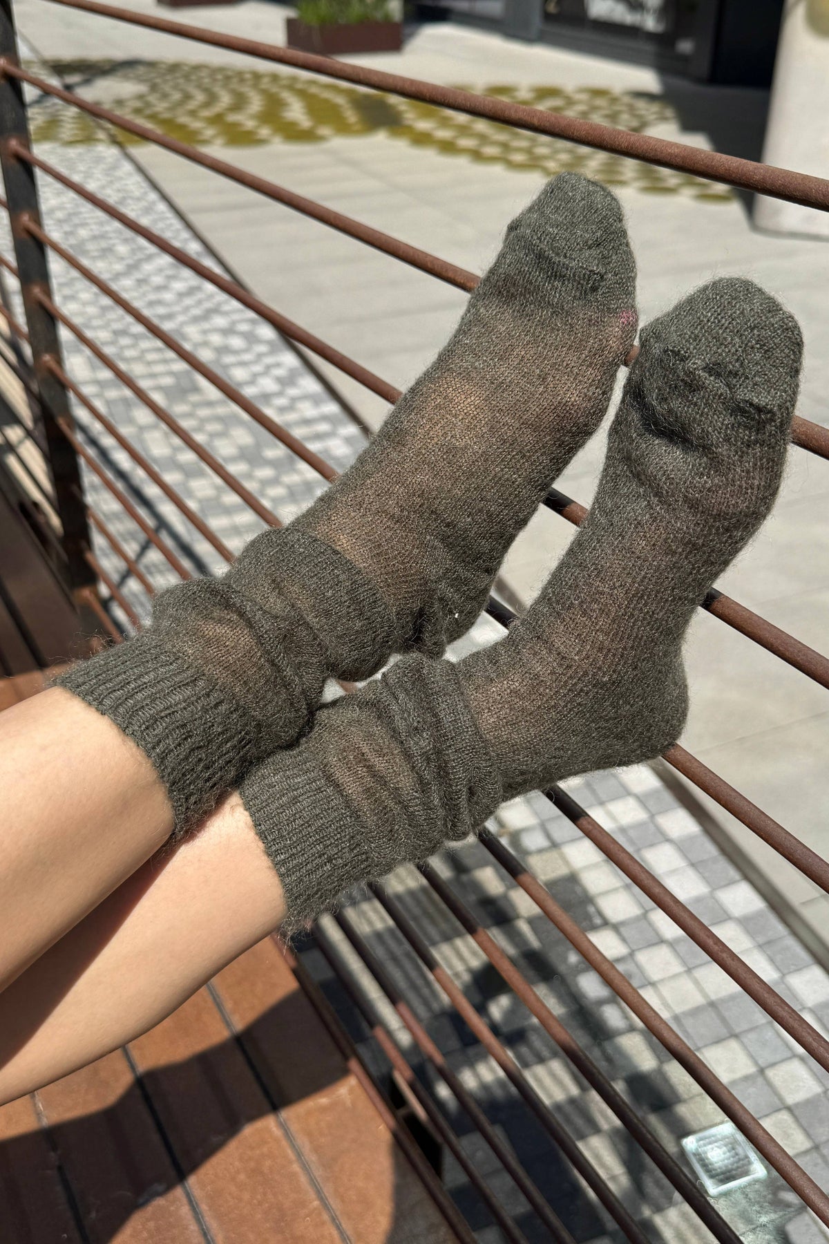 A pair of dark brown ribbed knit socks worn on feet resting on a metal railing outdoors.