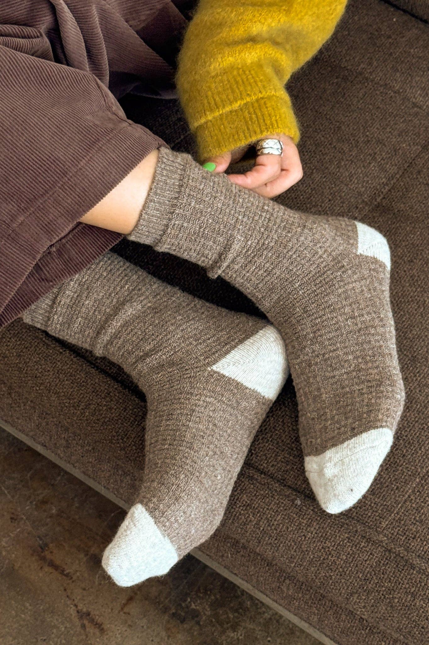 Person wearing brown socks with white toes and heels on a brown couch.